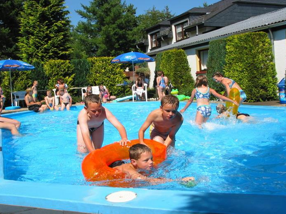 Kinderen spetteren en spelen met een opblaasband in het zonnige buitenzwembad van Feriendorf Felsenhof.