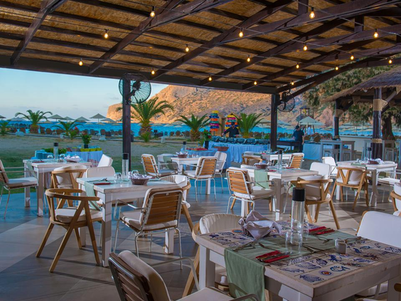 Het sfeervol verlichte terras van een restaurant bij Fodele Beach Resort in de avond, met gedekte tafels en uitzicht op zee.