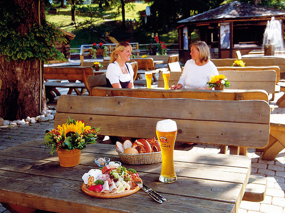 Gasten genieten van een hapje en een drankje, waaronder een pretzel en een glas bier, op het gezellige terras van het hotel in Garmisch-Partenkirchen.