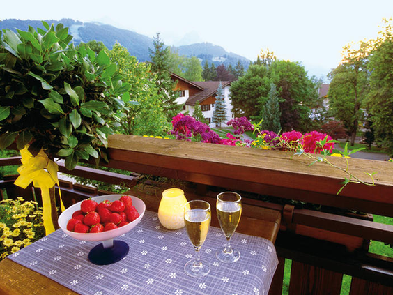 Een gezellig gedekte tafel met aardbeien en een drankje op een balkon met bloemen, met uitzicht op de bergen en het dorp Garmisch-Partenkirchen.