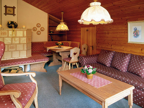De sfeervolle woonkamer van een appartement in Dorint Sporthotel Garmisch-Partenkirchen, ingericht in traditionele Beierse stijl met een houten zithoek en een tegelkachel.