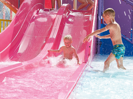Twee jongens hebben waterpret op een brede, roze glijbaan in het aquapark van Grecotel Club Marine Palace op Kreta.