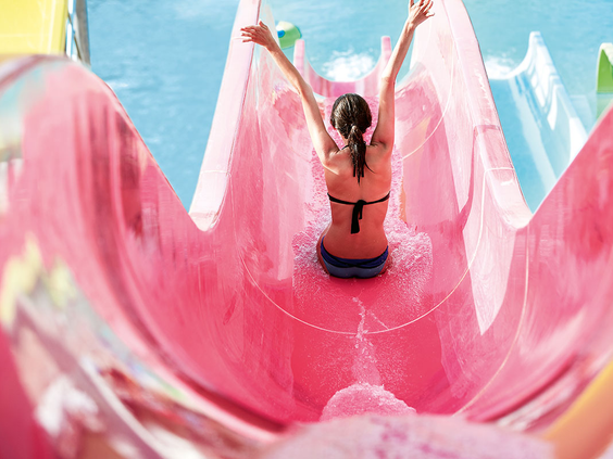 Een meisje glijdt met haar armen in de lucht door een spannende, roze trechterglijbaan in het aquapark van Grecotel Club Marine Palace.