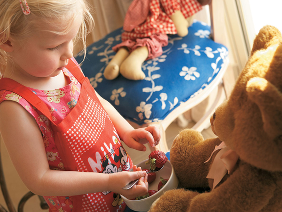 Een jong meisje deelt een schaaltje aardbeien met haar teddybeer in de gezellige familiekamer van Grecotel Club Marine Palace.