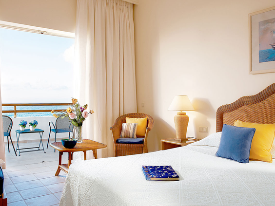 De lichte slaapkamer van een familiekamer bij Grecotel Club Marine Palace met een comfortabel bed en een balkon met prachtig uitzicht op de zee van Kreta.
