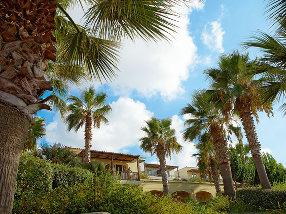 De sfeervolle, lichte gebouwen van Grecotel Club Marine Palace, prachtig gelegen tussen de hoge palmbomen en groene planten op Kreta.