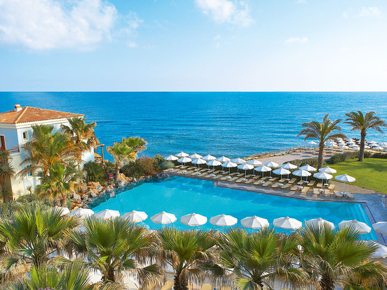 Het prachtige zwembad van Grecotel Club Marine Palace direct aan de zee, omringd door witte parasols, ligbedden en palmbomen op Kreta.