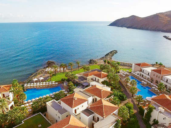 Luchtfoto van het uitgestrekte Grecotel Club Marine Palace resort, gelegen in een schitterende privébaai op Kreta, met diverse zwembaden en uitzicht op zee.