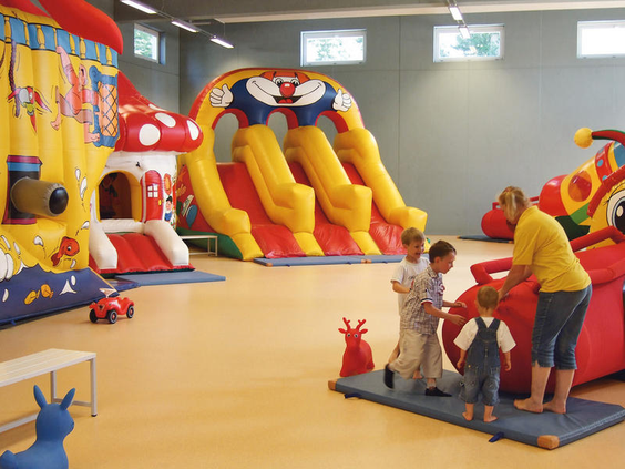 Kinderen spelen in de indoorspeeltuin van Hasseröder Ferienpark op een groot opblaasbaar speeltoestel met glijbanen.