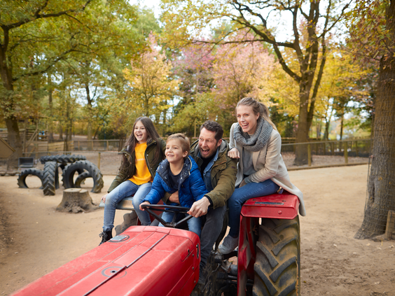 en lachend gezin met een jongen en een meisje zit op een rode tractor in een van de buitenspeeltuinen van Center Parcs Het Heijderbos.