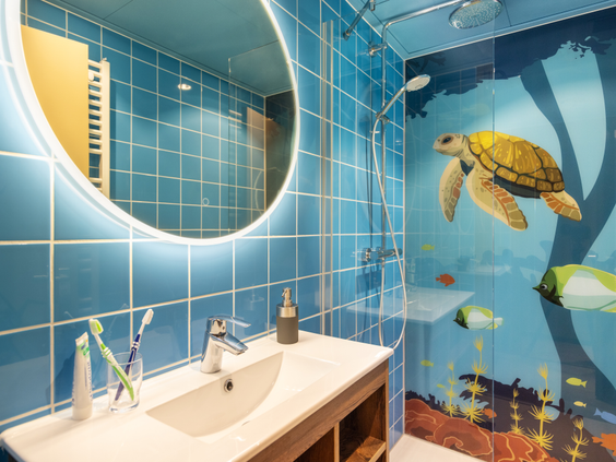 Een moderne badkamer in een cottage van Het Heijderbos met blauwe tegels en een muurschildering van een zeeschildpad en vissen in de douche.