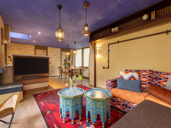 De gezellige woonkamer van een Premium cottage in Park Allgäu met Oosters tintje, met een comfortabele hoekbank, kleurrijke details en openslaande deuren naar het terras en het bos.