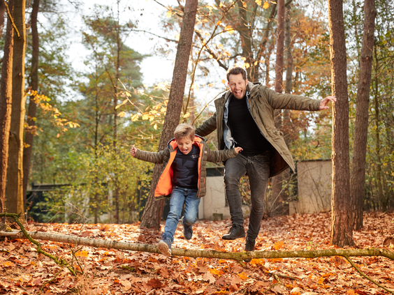 Een vader en zoon  lachend  in een herfstbos vol bladeren tijdens een wandeling in de omgeving van Center Parcs Het Heijderbos.