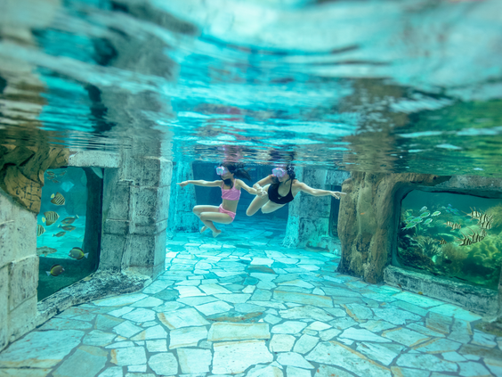Twee kinderen snorkelen onder water tussen de tropische vissen in het koraalbad van zwemparadijs Aqua Mundo in Center Parcs Het Heijderbos.