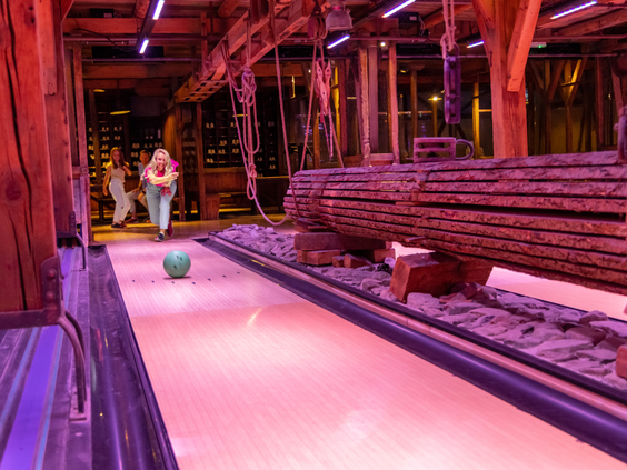 Mensen gooien een bal op de sfeervol verlichte bowlingbaan in de indoor Action Factory van Center Parcs Het Heijderbos.