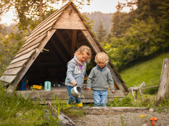 Twee kinderen spelen bij een kleine houten hut in de buitenlucht van Hilserhof, perfect voor fantasierijk spel op de boerderij.