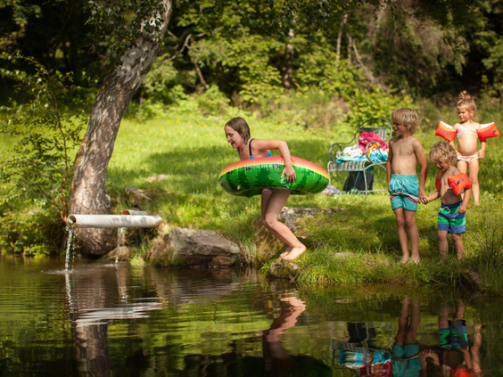 Kinderen met zwembandjes en opblaasfiguren spetteren en spelen in een natuurlijke waterplas bij Hilserhof, perfect voor waterpret.