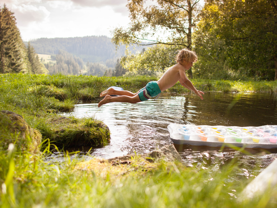 Een kind duikt enthousiast in een natuurlijke waterplas of beek bij Hilserhof, ideaal voor verkoeling en speelplezier op de boerderij.