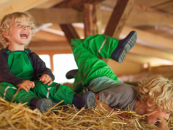 Twee lachende kinderen spelen vrolijk in het hooi op Hilserhof, een authentieke en leuke activiteit tijdens de boerderijvakantie.