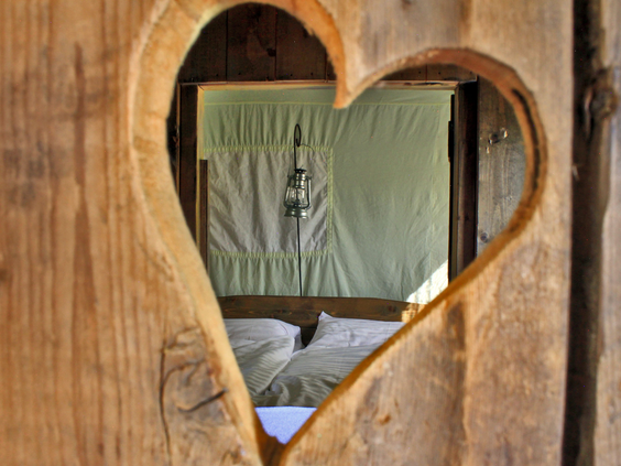 Uniek hartvormig raam met uitzicht op een slaapplek in de sfeervolle accommodaties van Hohenwarter Seehof, voor een romantische en gezellige familiesfeer.