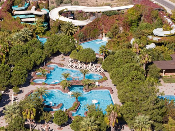 Overzicht van de prachtig aangelegde lagune-stijl zwembaden en waterglijbanen, omgeven door groene bomen bij Hotel Ali Bey Club.