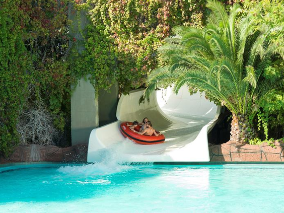 Twee personen in een opblaasbare band komen met een grote plons uit een brede, witte trechterglijbaan in het waterpark van Ali Bey Club.