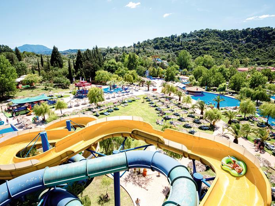 Weids overzicht van het Aqualand waterpark op Corfu met talloze kleurrijke waterglijbanen, zwembaden en groene heuvels op de achtergrond.