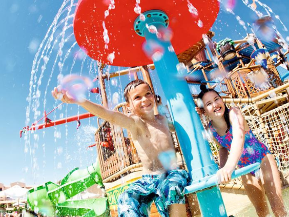 Lachende kinderen die volop plezier hebben met waterstralen en sproeiers in de vrolijke waterspeeltuin van het Aqualand waterpark.