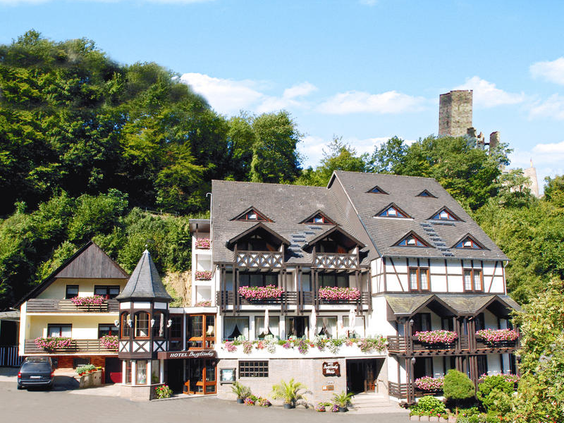 Hotel Burgfrieden, een charmant gebouw in traditionele stijl, gelegen tegen een groene heuvel met een indrukwekkende kasteelruïne op de achtergrond, in de Moezelstreek.