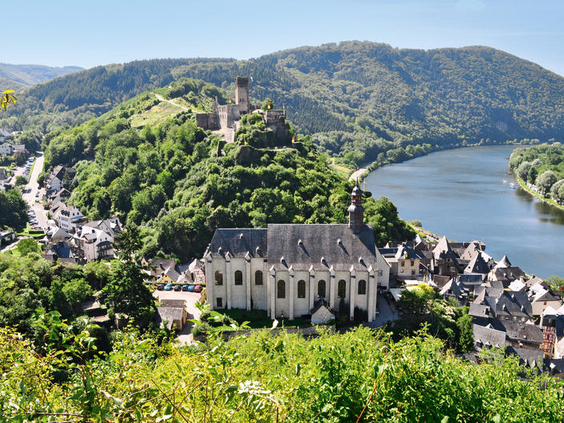 Panoramisch overzicht van het schilderachtige landschap van de Moezelstreek, met de rivier, een charmant dorp, groene heuvels en een imposant kasteel op een rots.