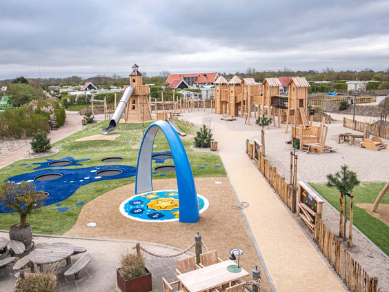 Overzicht van de grote buitenspeeltuin van zand en hout met klimtoestellen en trampolines bij Strandpark De Zeeuwse Kust.