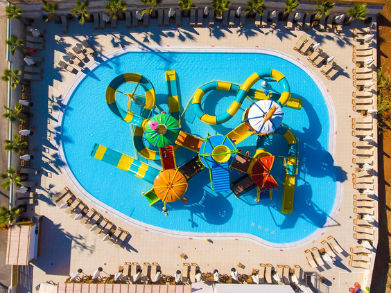 Luchtfoto van het kleurrijke waterspeelparadijs voor kinderen, vol met glijbanen, sproeiers en speeltoestellen in het water.