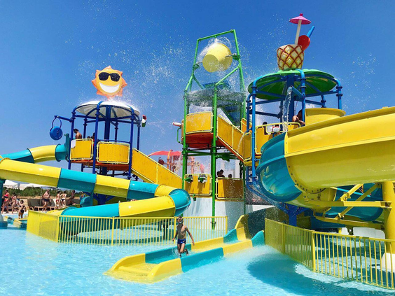 Kleurrijk waterspuitpark voor kinderen met kleine glijbanen, een ananas-fontein en een lachende zon-decoratie in het waterpark.