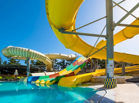 Een kluwen van gele en kleurrijke waterglijbanen die uitkomen in het zwembad van het aquapark bij Hotel Gouves Waterpark Holiday Resort.