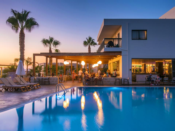 Sfeervol verlicht zwembad in de avond bij Hotel Gouves Waterpark Holiday Resort, met een gezellig terras en palmbomen.