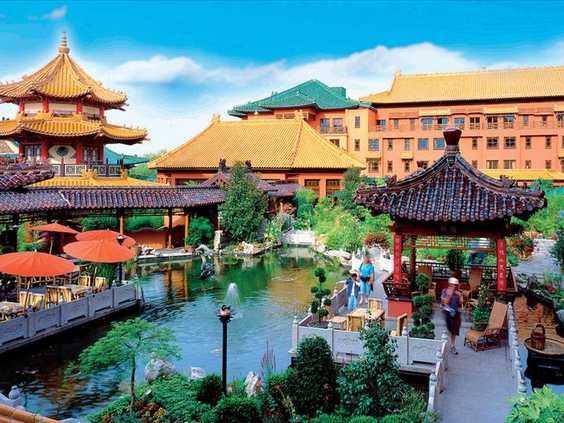 Overzicht van Hotel Ling Bao en de omliggende Aziatische tuinen, met een brug over de vijver en Chinese pagodes onder een blauwe lucht.