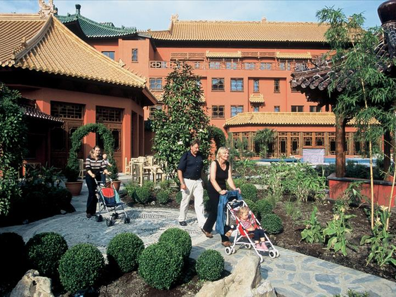 Een gezin met kinderwagens wandelt over een pad door de prachtig aangelegde, groene binnentuin van Hotel Ling Bao.