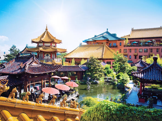 Zonnig aangezicht van Hotel Ling Bao bij Phantasialand, met de kenmerkende Chinese architectuur, daken en een terras aan het water.