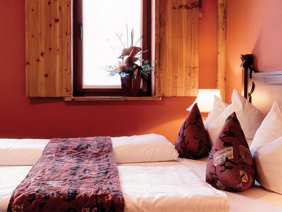 Sfeervol opgemaakt tweepersoonsbed in een familiekamer van Hotel Ling Bao, met decoratie in Aziatische stijl en warme, rode kleuren.