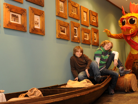 Twee jongens spelen in een houten boot in de speelruimte van Hotel Ling Bao, met de hotelmascotte die toekijkt.