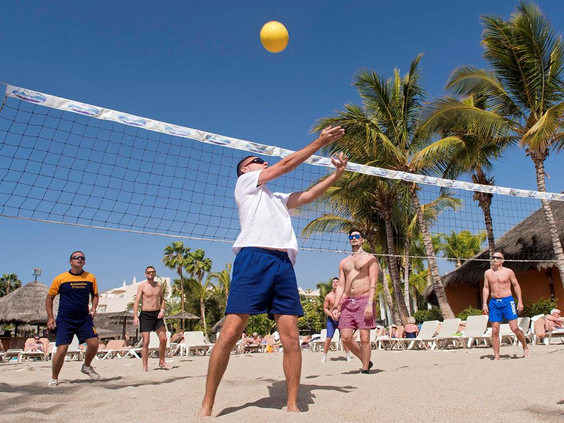 Vakantiegangers die een potje beachvolleybal spelen op het aangelegde strand van Maspalomas Princess, met een net en palmbomen.