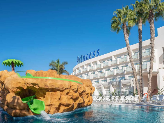 Een kleine, groene kinderglijbaan die uit een kunstmatige rots komt en uitmondt in het zwembad van Maspalomas Princess