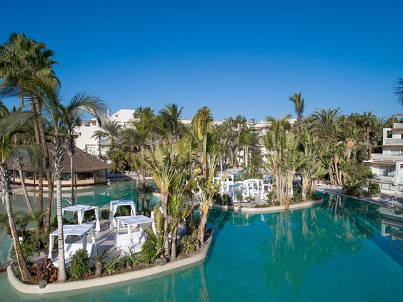 Overzicht van het enorme zwemparadijs van Hotel Maspalomas Princess, met eilandjes vol palmbomen en luxe witte cabana's in het water.