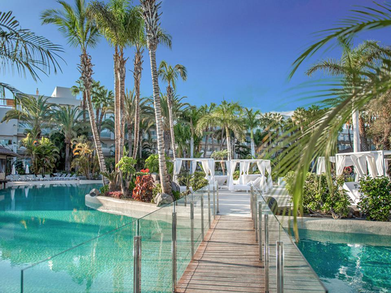 Het tropische zwemparadijs van Maspalomas Princess met een houten brug over het helderblauwe water en luxe witte cabana's.