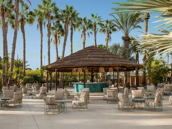 De tropische loungebar met rieten dak bij Hotel Maspalomas Princess, omringd door palmbomen en comfortabele zitjes.