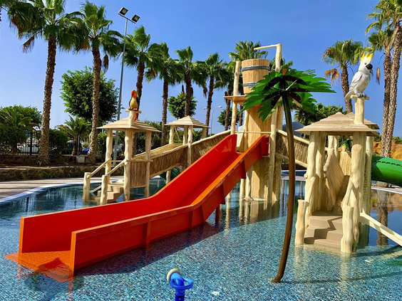 Het kleurrijke waterpark voor kinderen bij Maspalomas Princess, met een brede rode glijbaan, een speelfort en palmbomen.