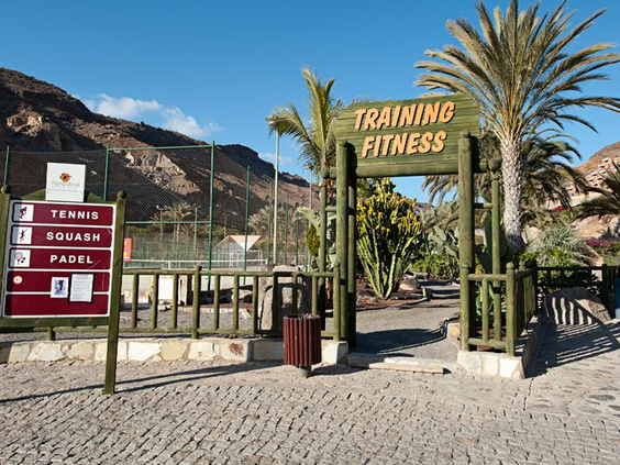 De ingang van de sportfaciliteiten bij Hotel Paradise Lago Taurito, met tennisbanen en een bord voor andere sporten zoals padel.