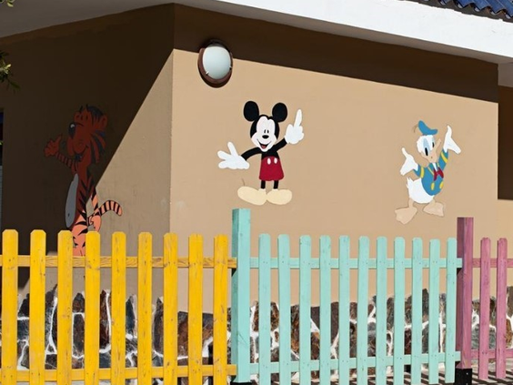 De vrolijke buitenkant van de kidsclub bij Hotel Paradise Lago Taurito, met een kleurrijk hek en bekende tekenfilmfiguren zoals Mickey Mouse op de muur.