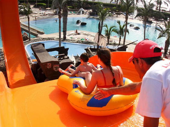 Een familie in een opblaasband krijgt een duwtje van de badmeester om van de brede oranje familieglijbaan te glijden in waterpark Paradise Lago Taurito.