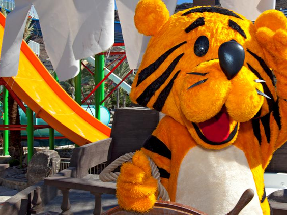 De vrolijke tijger mascotte van de kinderclub van Hotel Paradise Lago Taurito zwaait enthousiast bij het waterpark.